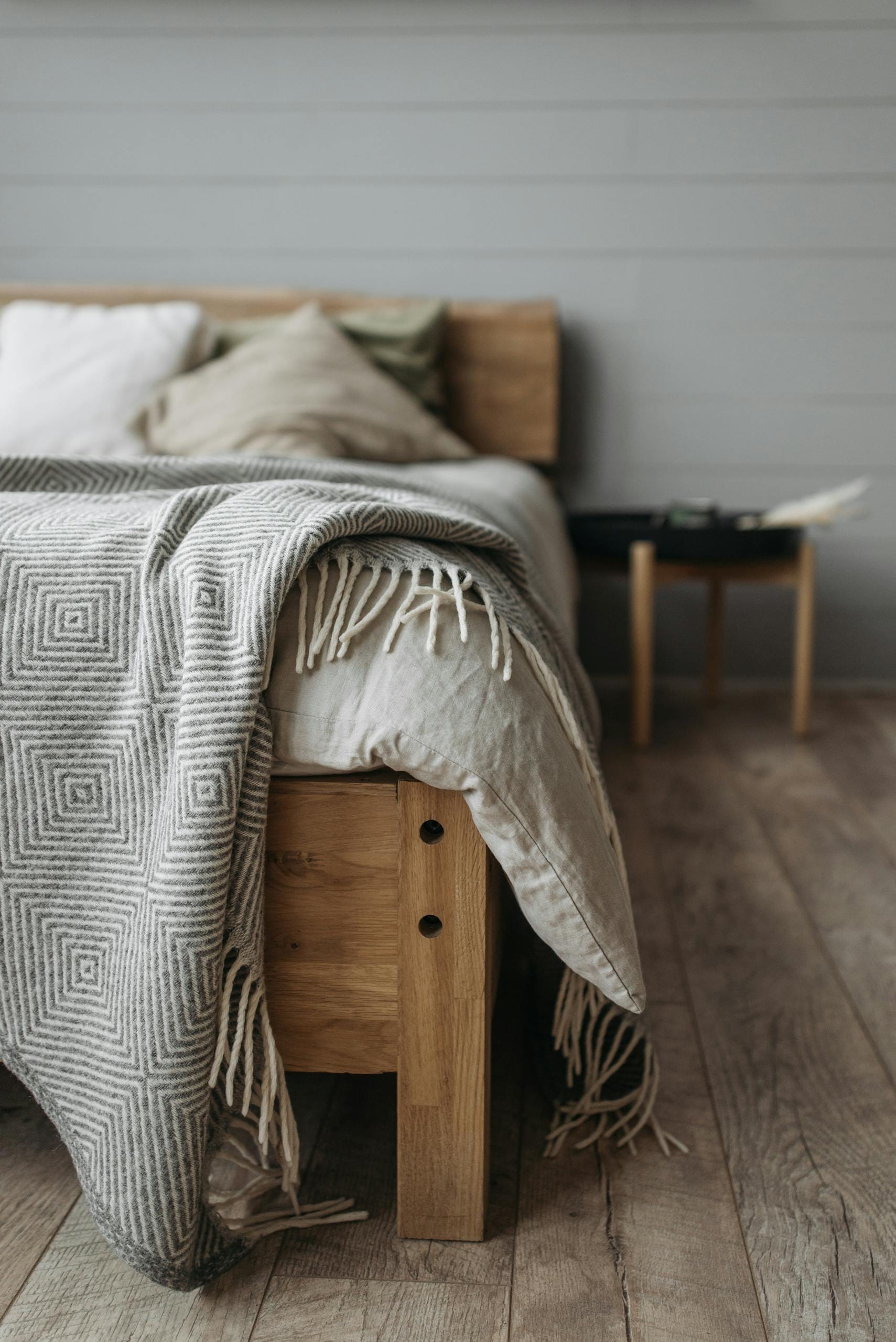 A cozy bedroom with a wooden bed, pillows, and a patterned blanket on a wooden floor.