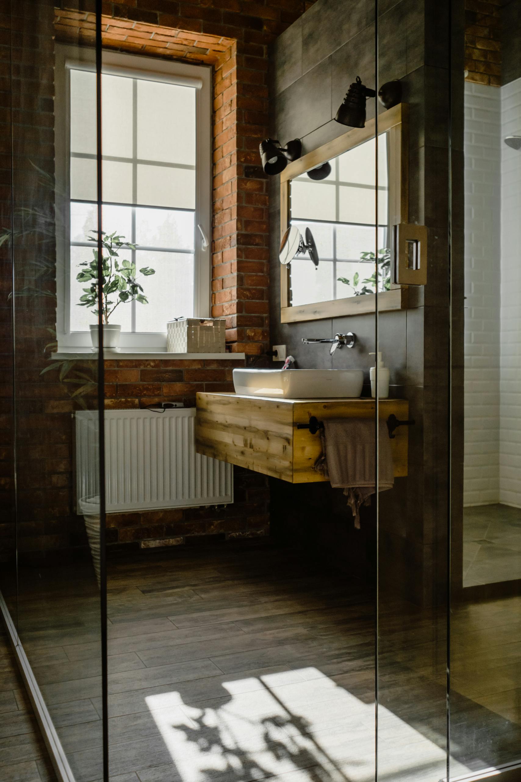 Modern bathroom with glass door, wooden sink, and natural brick wall.