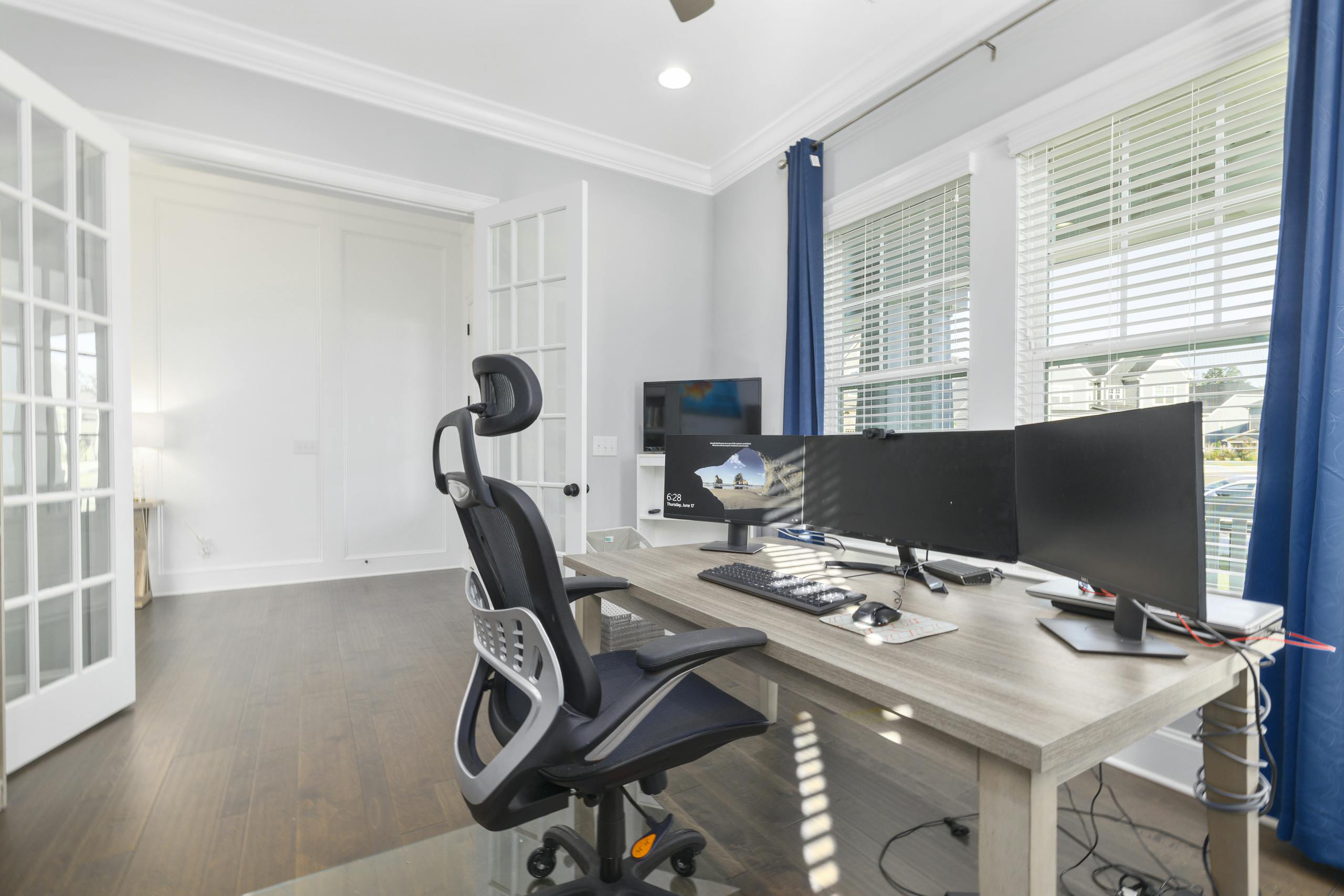 Brightly lit home office featuring an ergonomic chair, dual monitors, and a spacious desk setup for productivity.